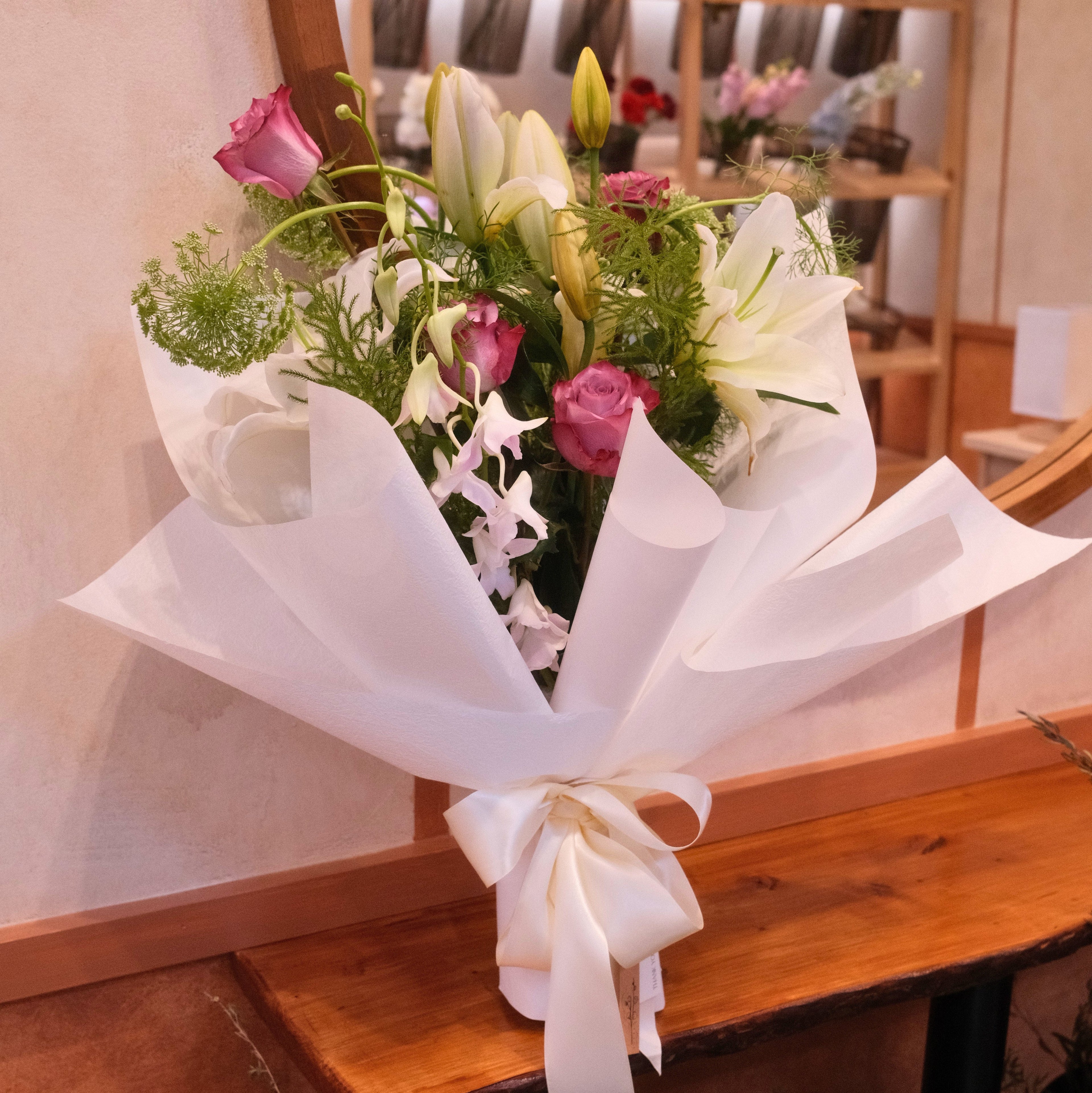 Bouquet of flowers with lilies, roses and orchid wrapped in white paper with a bow as gift made by Hanaya Flora, Surry Hills, Sydney.