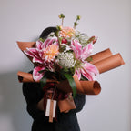 Japanese Style bouquet of Double Oriental Lily - Rose Lily flowers wrapped in brown wrapping paper with a red ribbon on a white background by Hanaya Flora, based in Sydney.