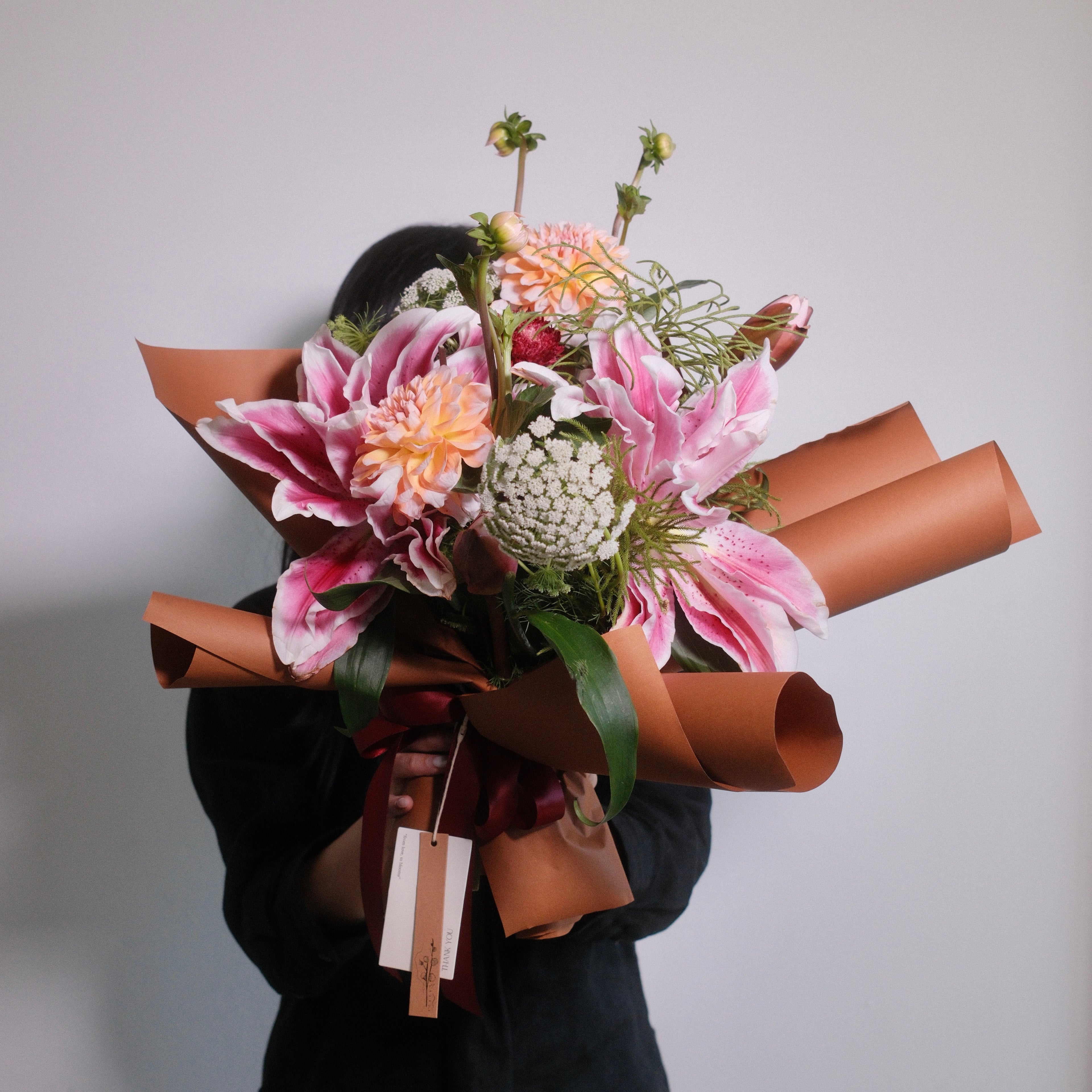 Japanese Style bouquet of Double Oriental Lily - Rose Lily flowers wrapped in brown wrapping paper with a red ribbon on a white background by Hanaya Flora, based in Sydney.