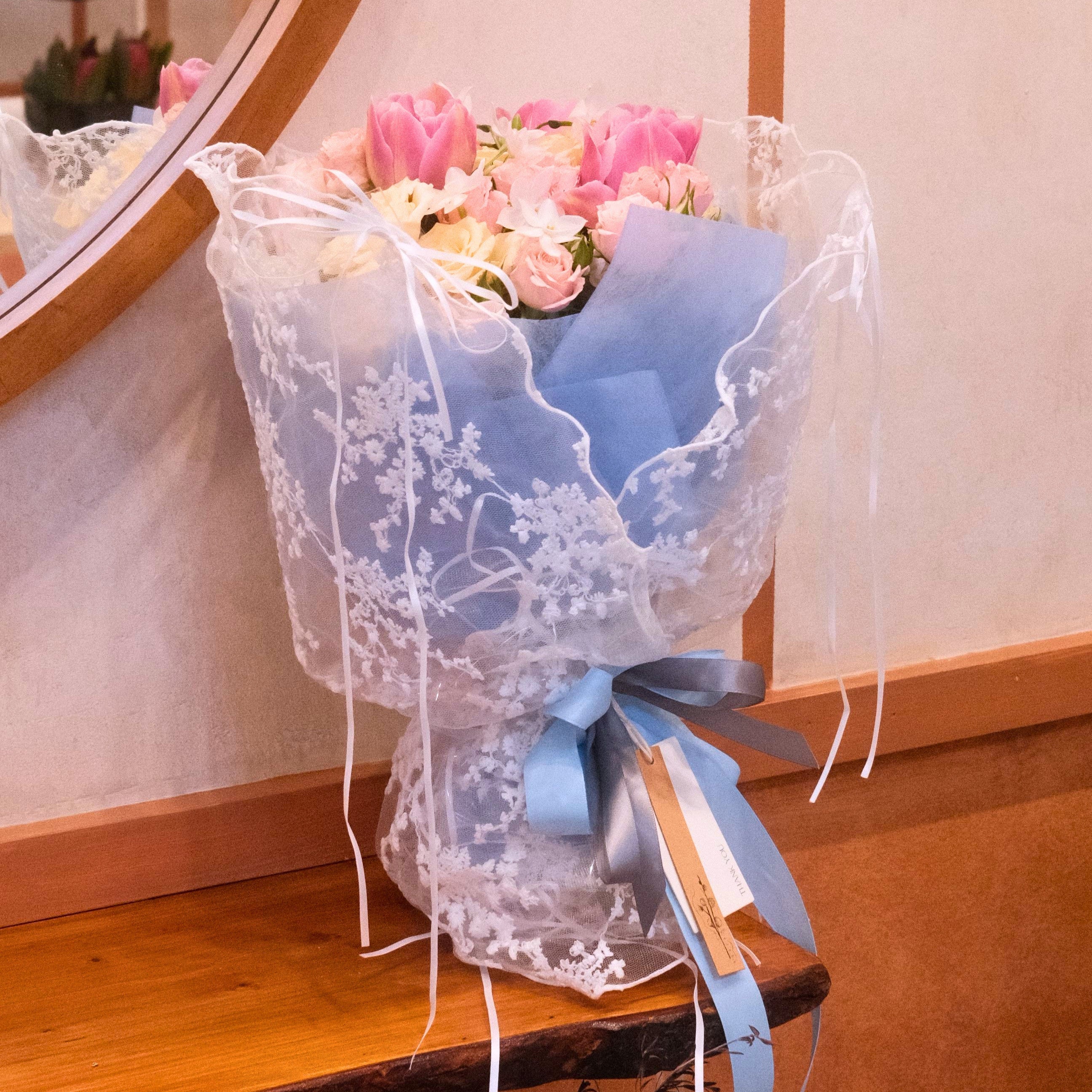 Bouquet of pink and white flowers such as tulip and roses that wrapped in lace wrapping designed by Hanaya Flora, Surry Hills, Sydney. 