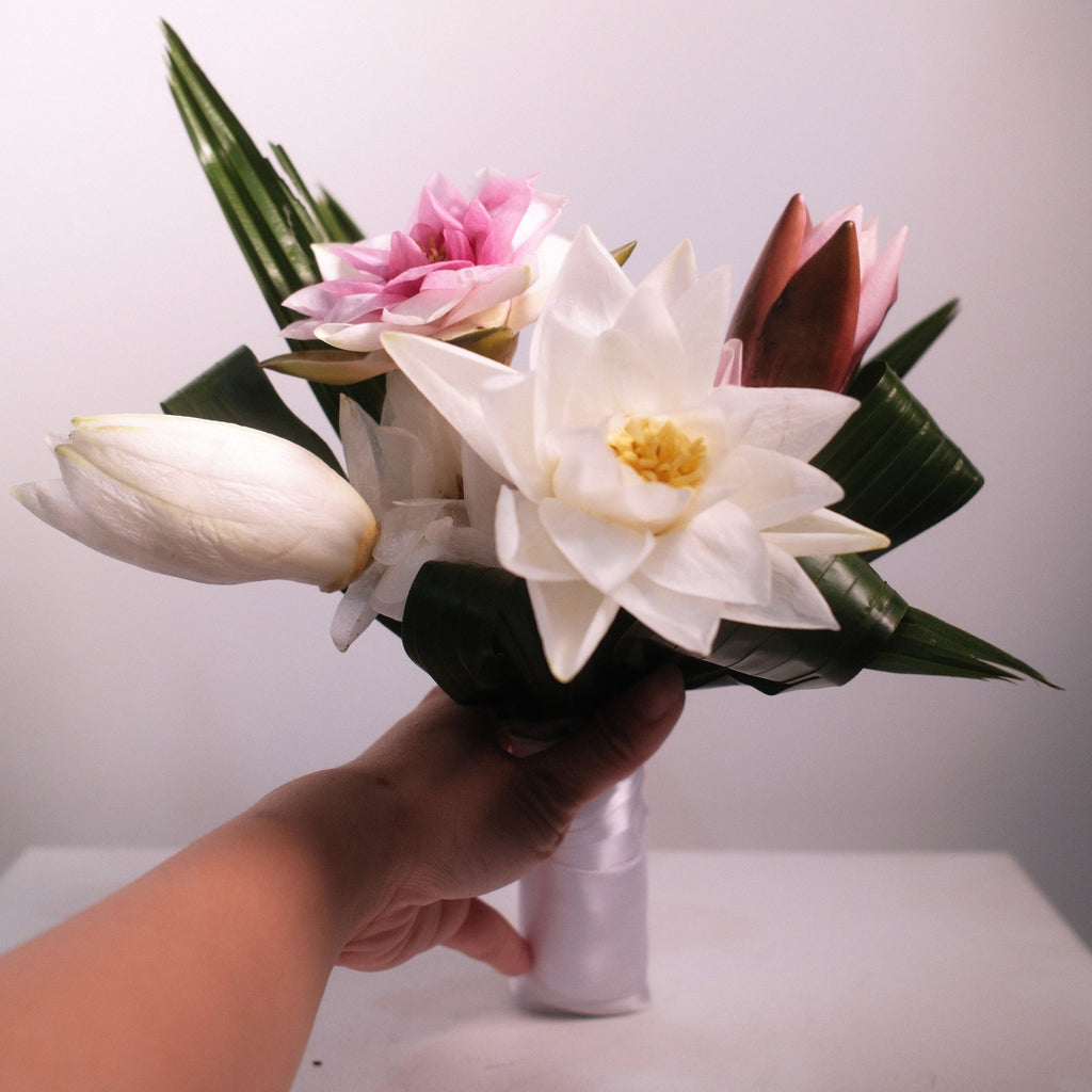 Close-up of white lotus bridal bouquet with pink lotus accent and folded palm leaves