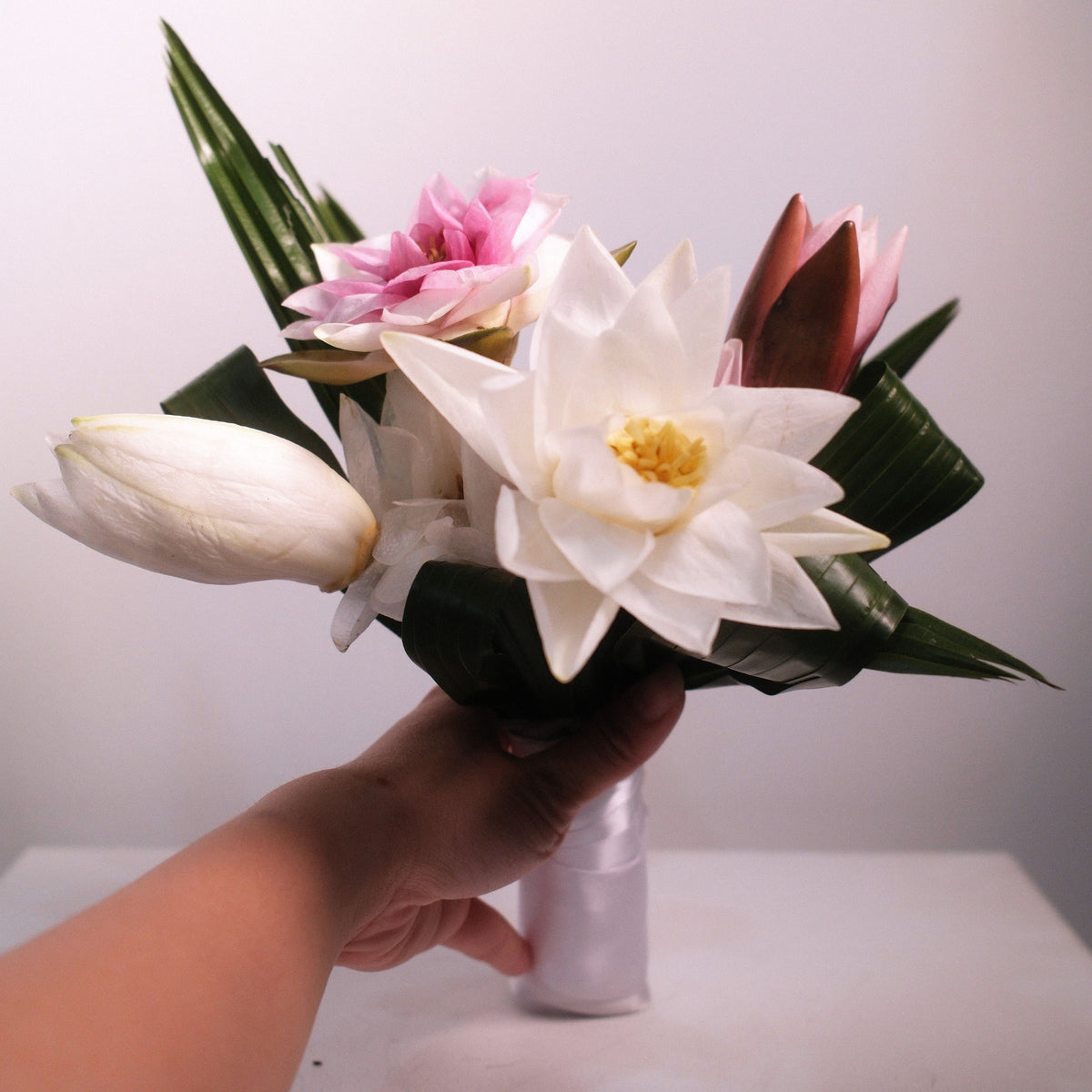 Close-up of white lotus bridal bouquet with pink lotus accent and folded palm leaves