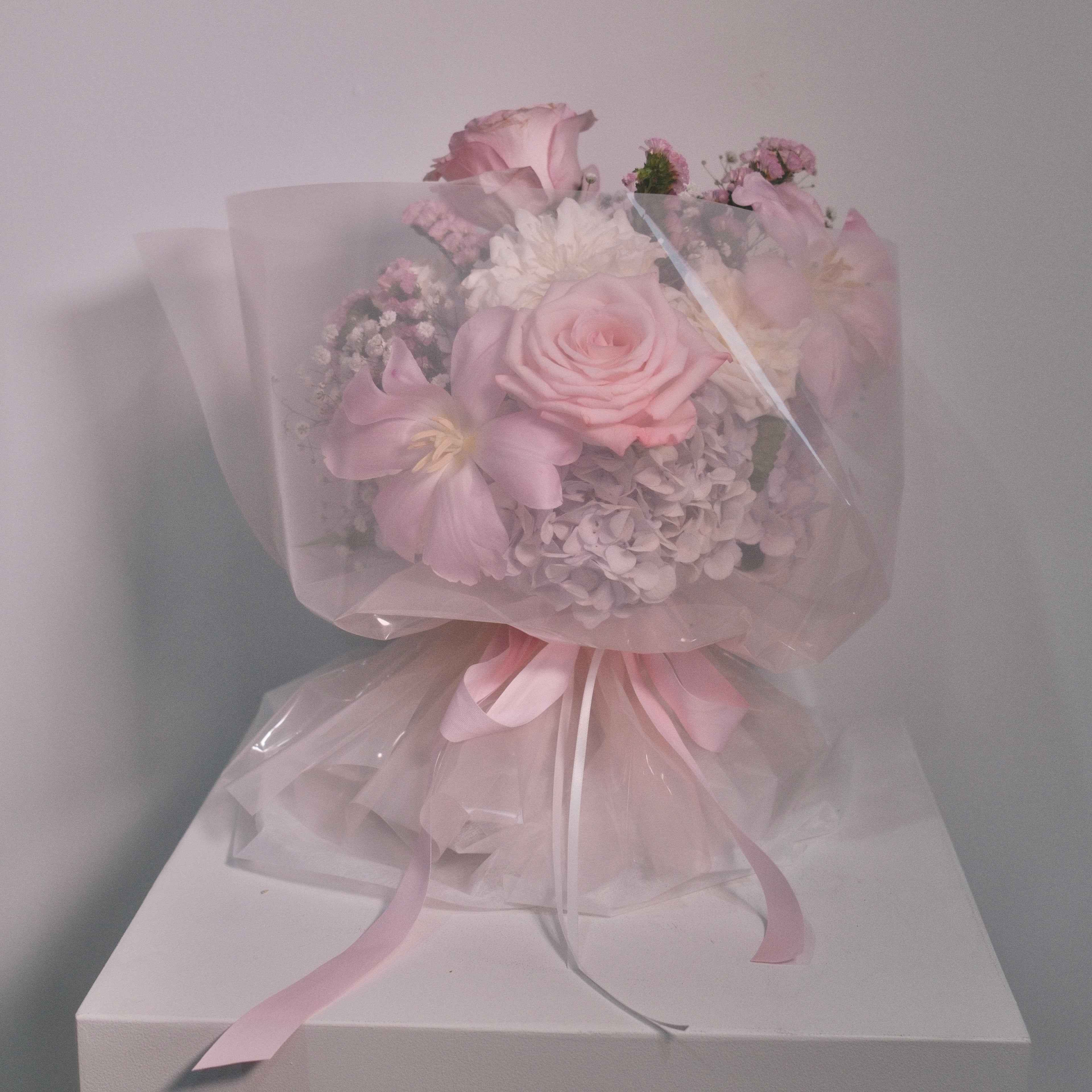 Cute bouquet of soft pink roses and delicate small white roses with fluffy hydrangeas, filled up with baby breath and statices wrapped in pink cellophane paper with a neat pink ribbon bow by Hanaya Flora, based in Sydney.