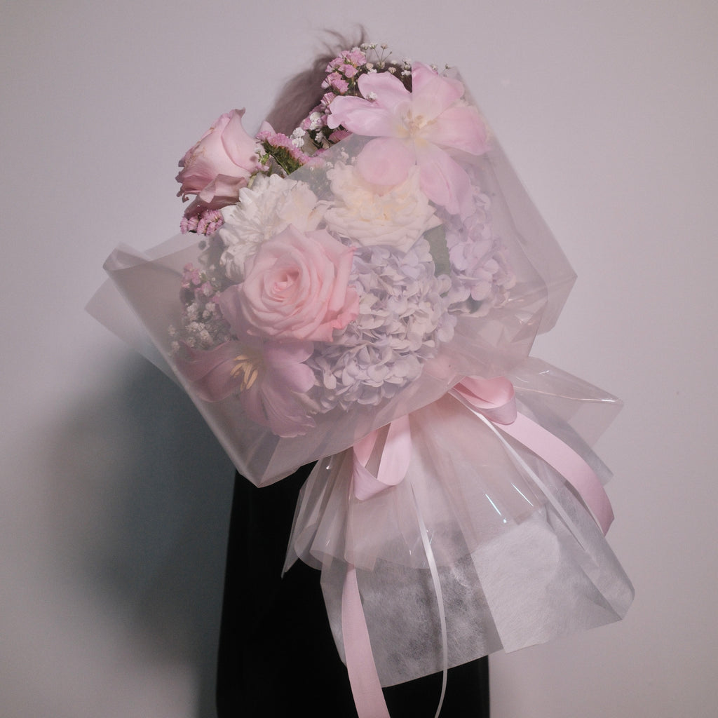 Close-up of the First Love bouquet in translucent wrap, held by a florist