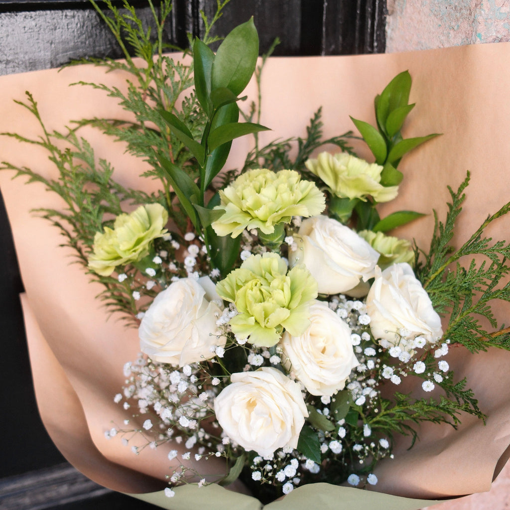 Close-up of white roses, sage green carnations and baby's breath in the Gentle Remembrance sympathy bouquet