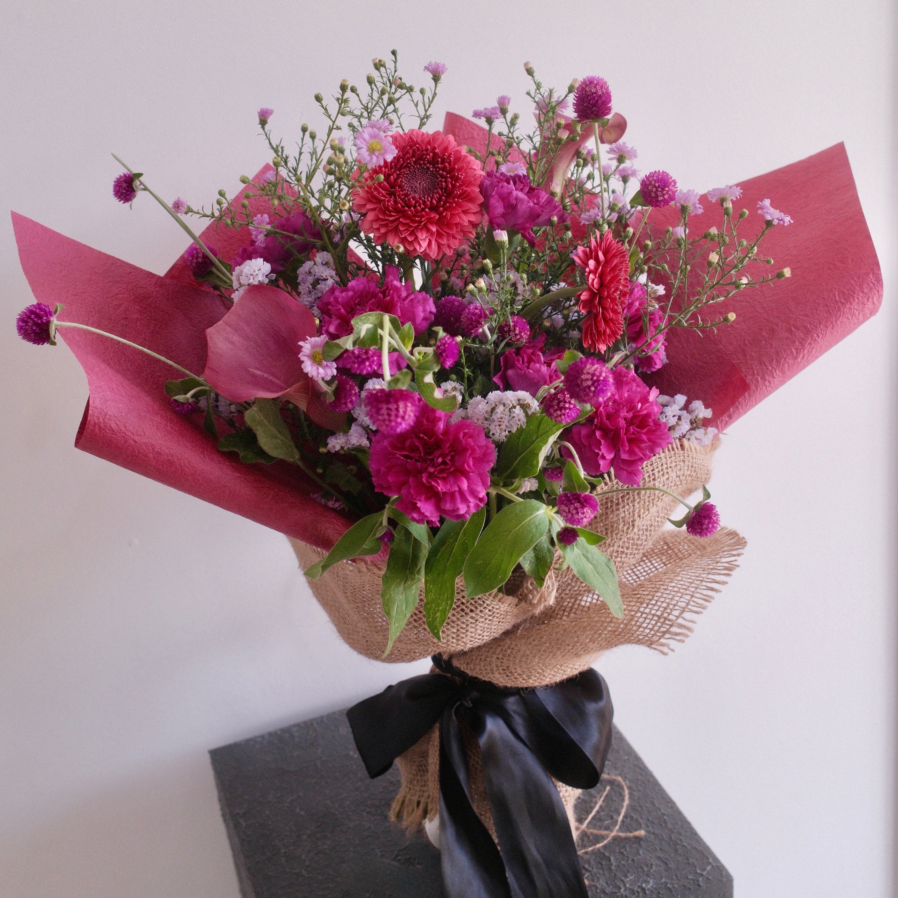 Bouquet of purple flowers wrapped with cerise paper with black ribbon, perfect for celebrating a graduation made by Hanaya Flora, based in Sydney. 