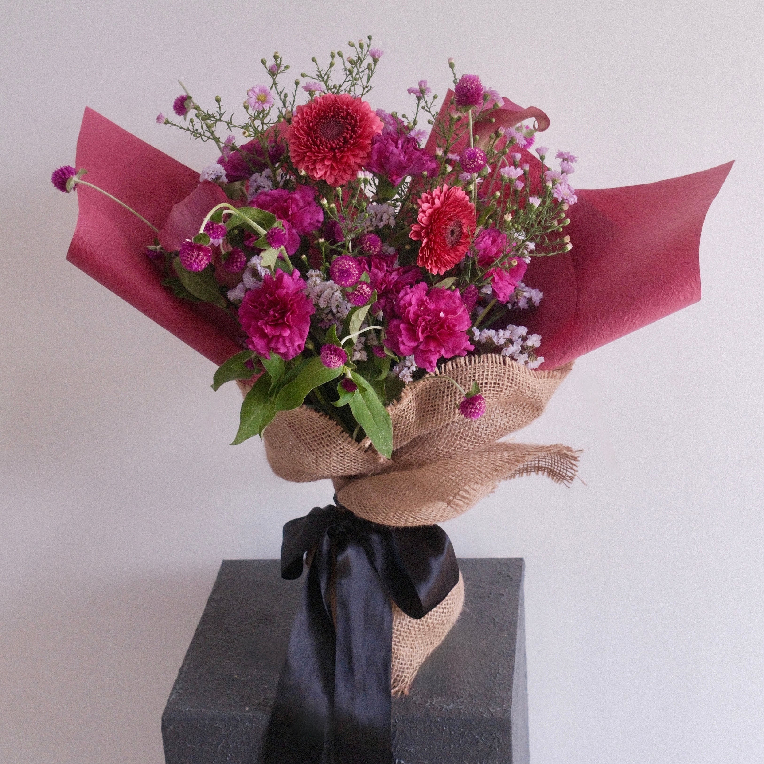 Bouquet of purple flowers wrapped with cerise paper with black ribbon, perfect for celebrating a graduation made by Hanaya Flora, based in Sydney. 