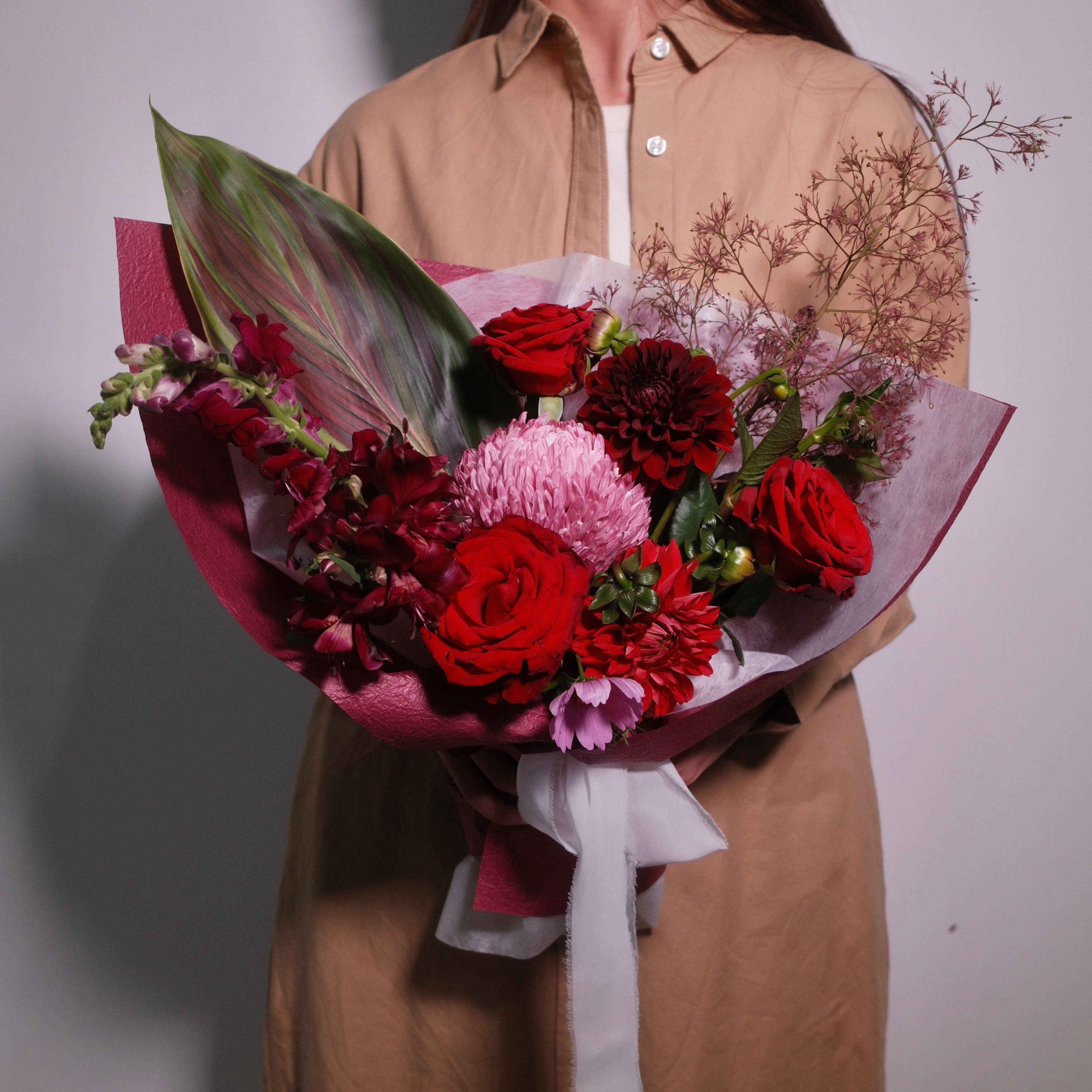 Bouquet of premium red roses and wild flowers wrapped in red paper with a white bow, by Hanaya Flora, Surry Hills, Sydney.