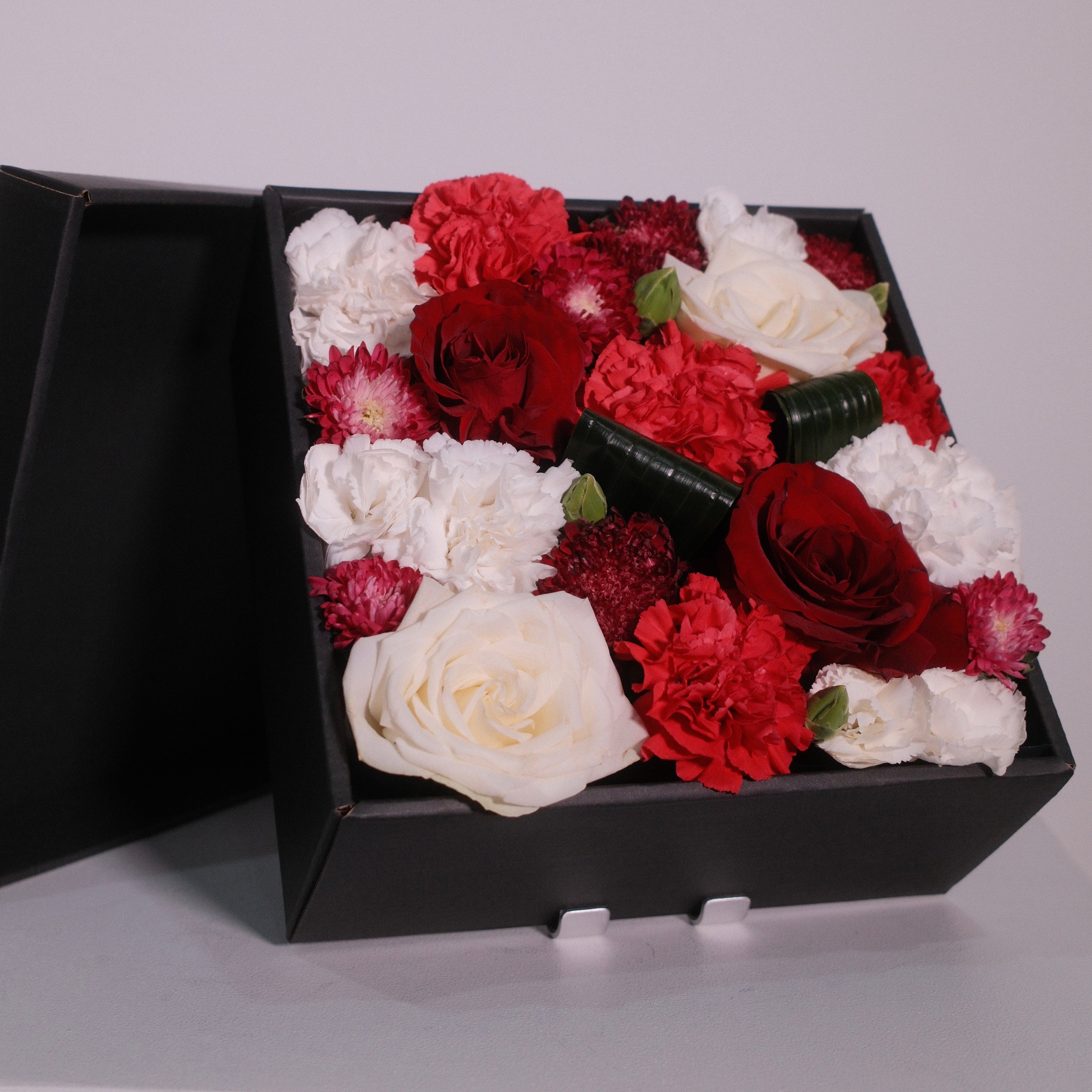 Close-up of the Hanaya Box Red with red roses, carnations and scabiosa