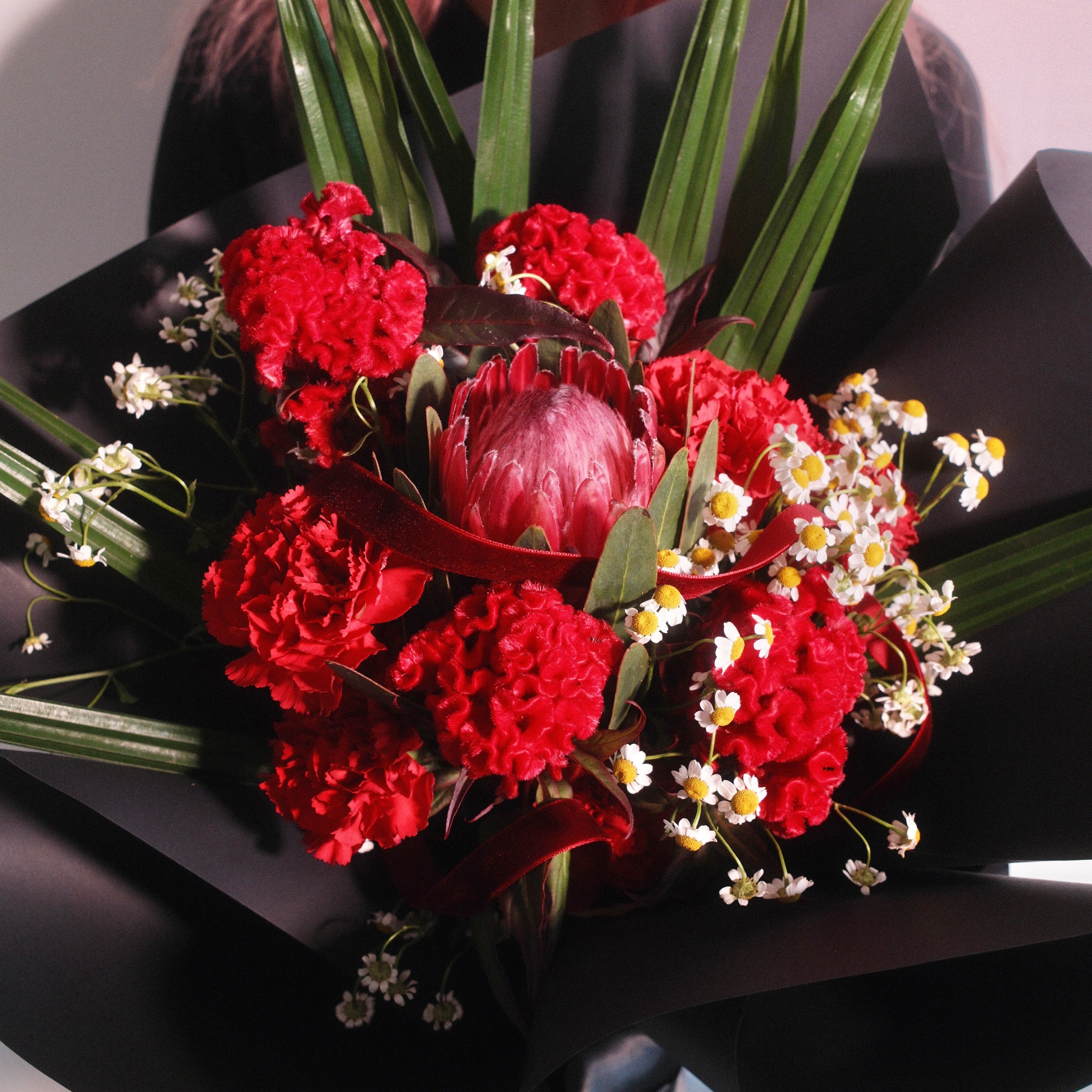Close-up of Kunerai Grace bouquet with red celosia, carnations and king protea