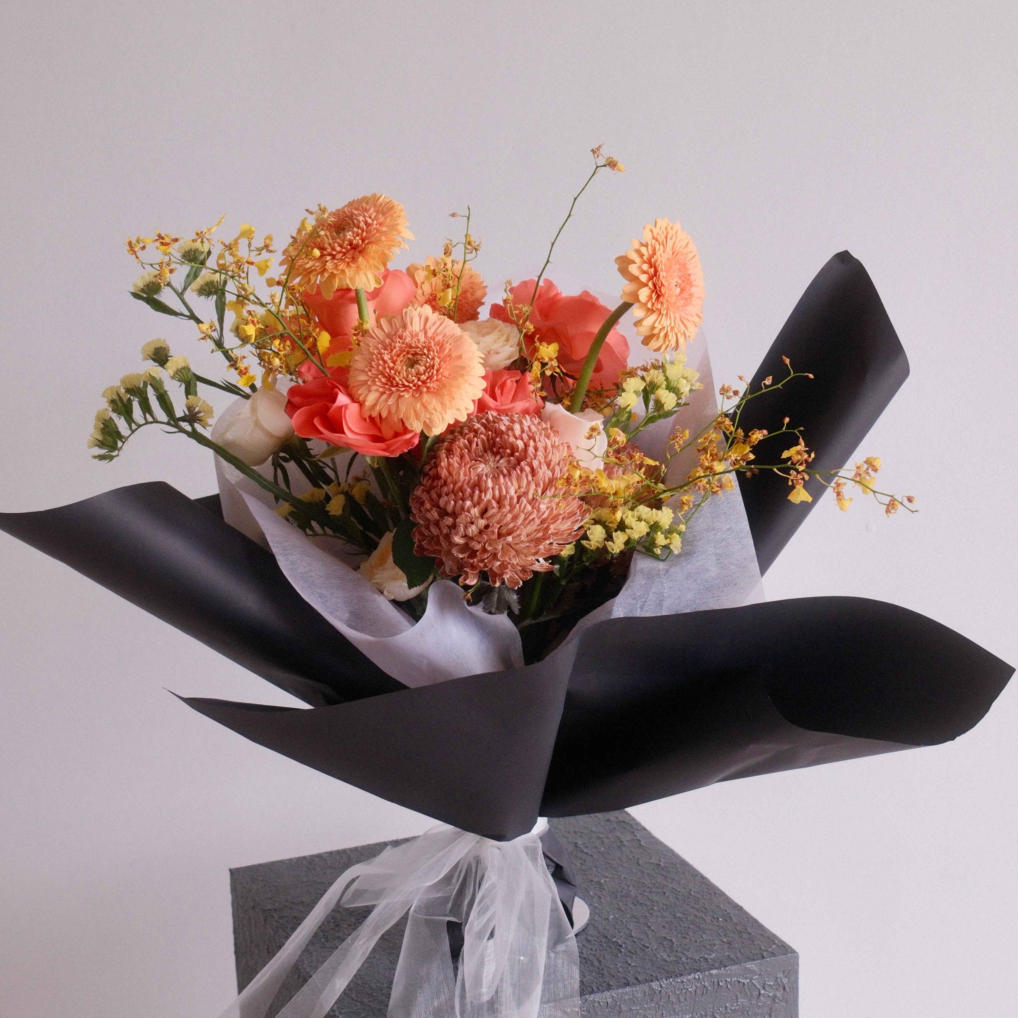 Bouquet of flowers orange rose, gerbera, and chrysanthemum wrapped in black paper with a white ribbon made by Hanaya Flora, Sydney, Surry Hills