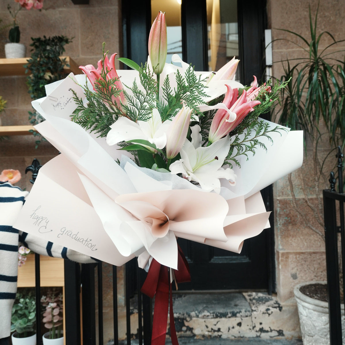 Mirai Grace pink and white lily graduation bouquet with "happy graduation" wrapping, outside a Sydney sandstone shopfront