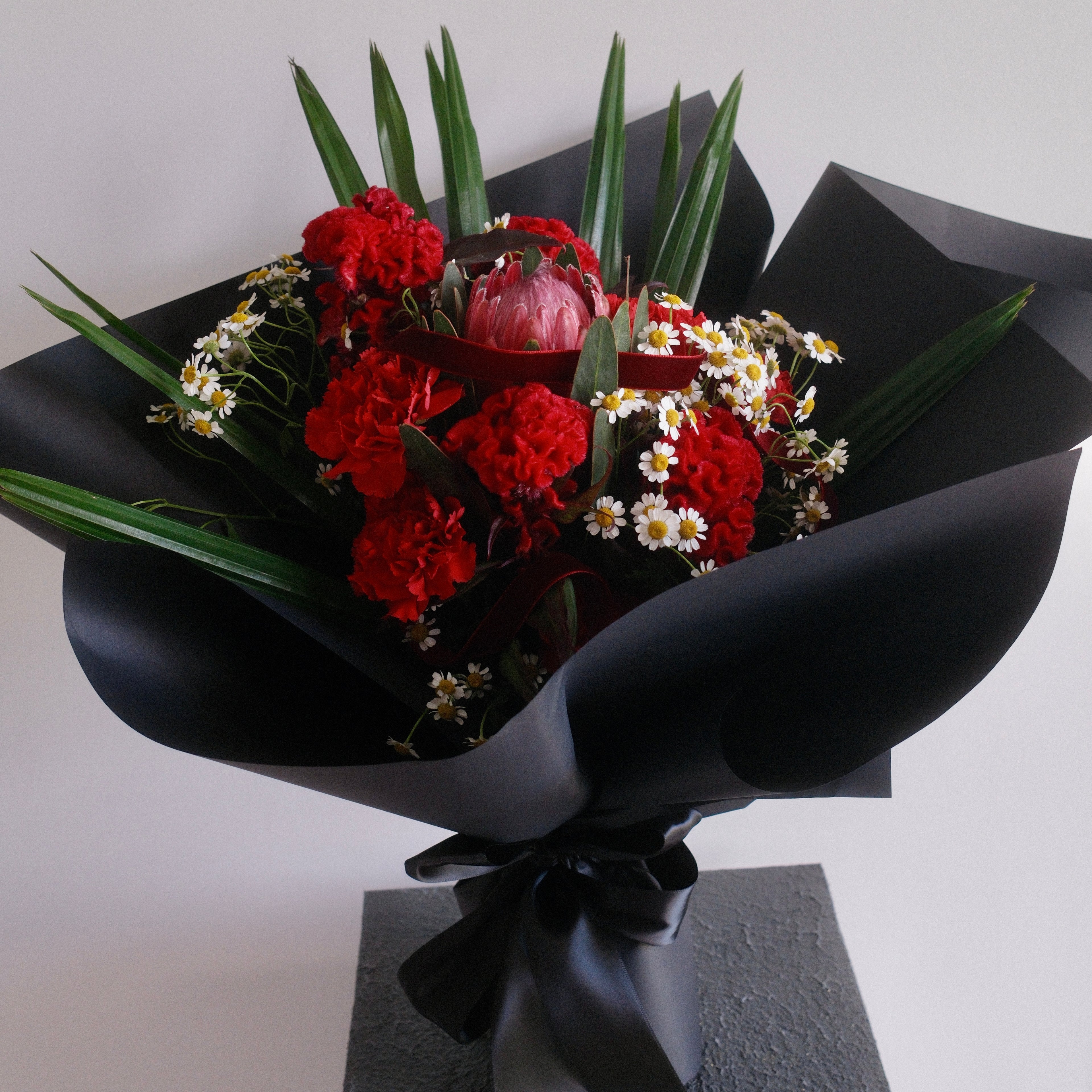 Bouquet of flowers with red carnation and chamomile, wrapped in premium black paper by Hanaya Flora, Surry Hills, Sydney. 