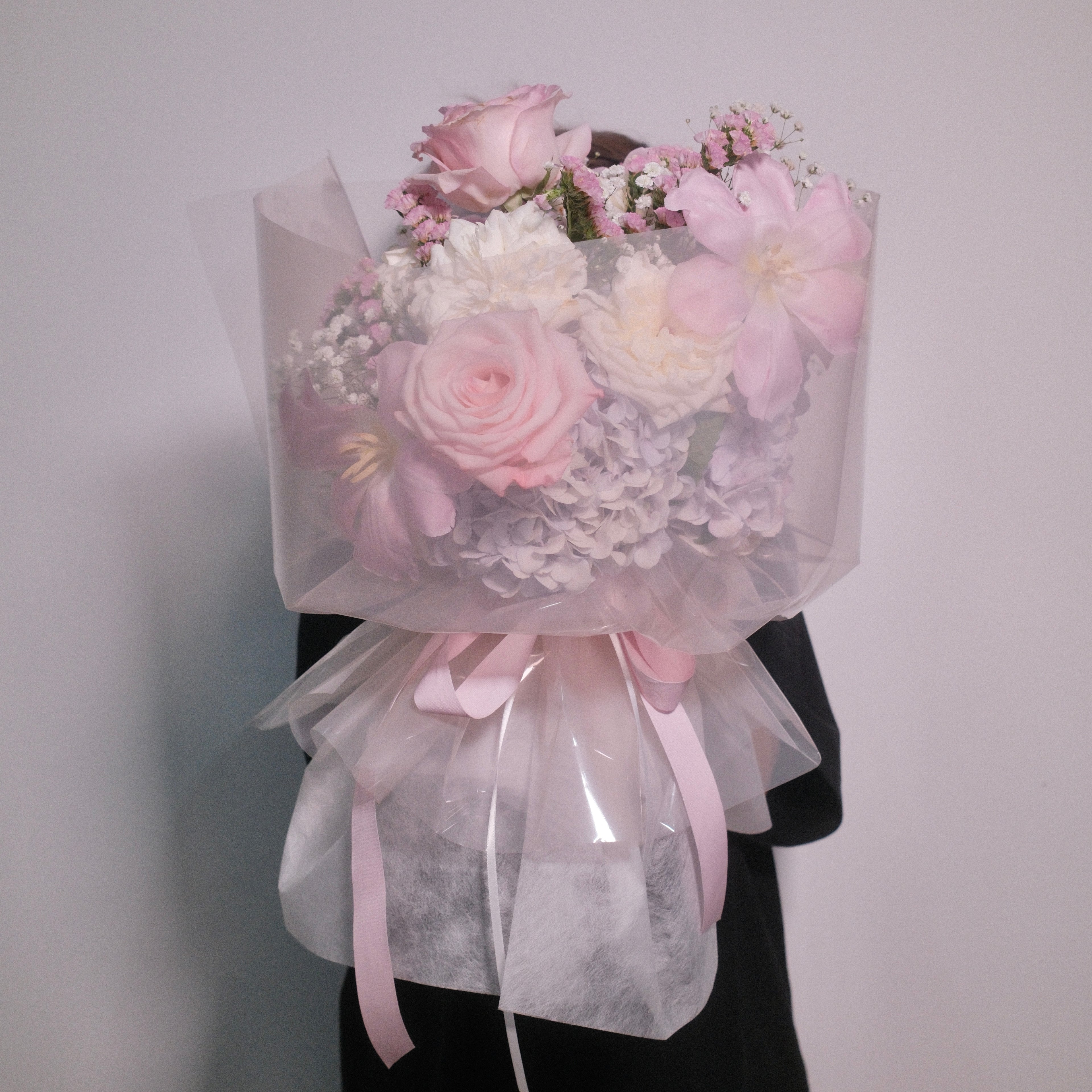 Cute bouquet of soft pink roses and delicate small white flowers with fluffy hydrangeas, wrapped in pink cellophane paper with a neat pink ribbon bow by Hanaya Flora, based in Sydney.