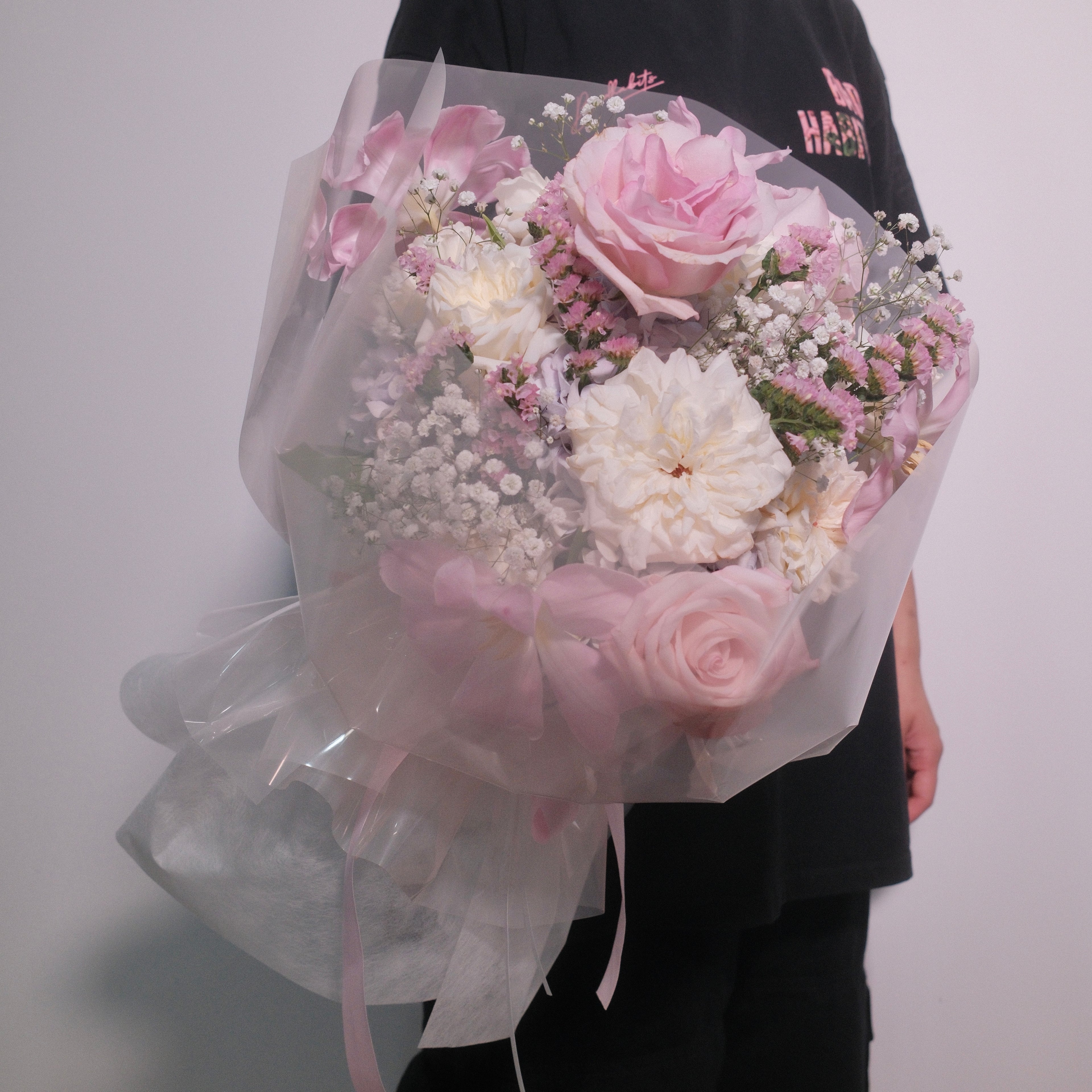 Cute bouquet of soft pink roses and delicate small white roses with fluffy hydrangeas, filled up with baby breath and statices wrapped in pink cellophane paper with a neat pink ribbon bow by Hanaya Flora, based in Sydney.
