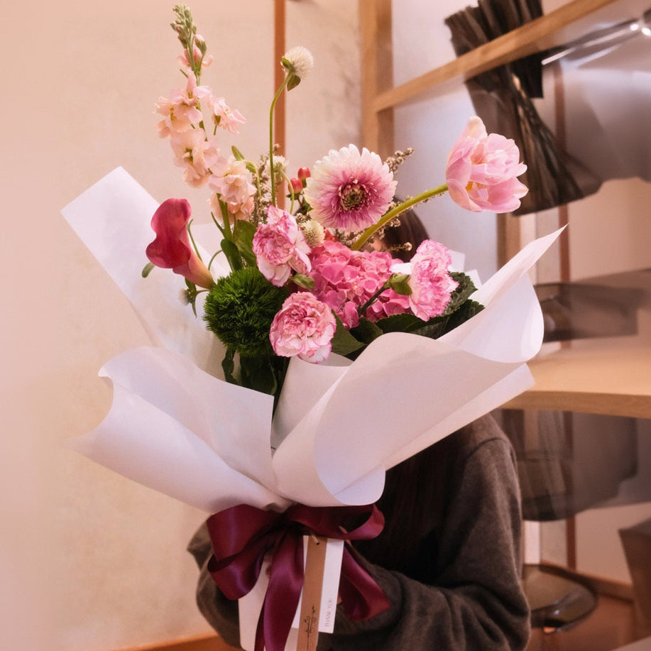 Bouquet of mixed pink flowers with tulip, calla lily, gerbera, hydrangea wrapped in white paper with a red ribbon made by Hanaya Flora, Surry Hills, Sydney.