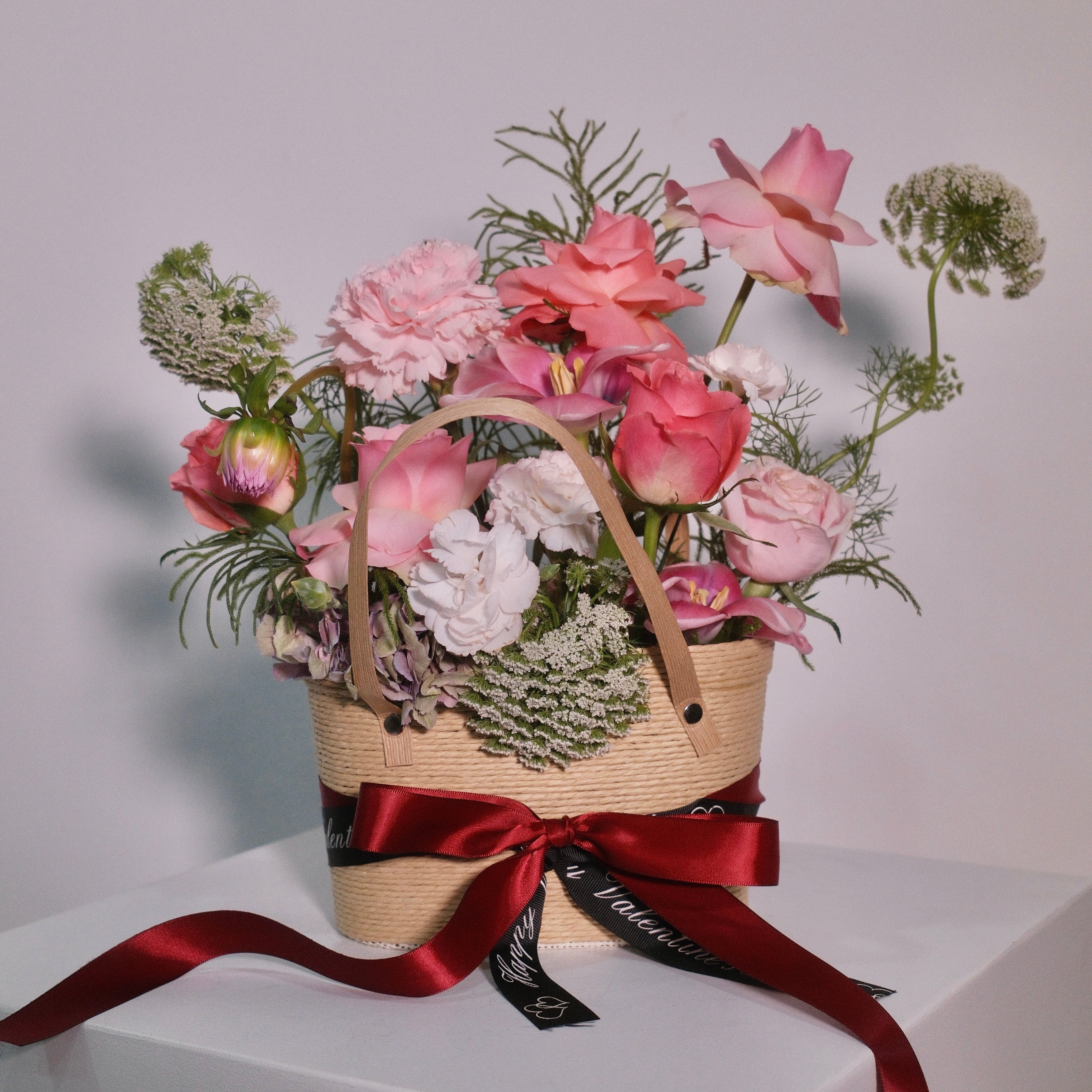 Floral arrangement with soft pink roses in a woven basket with a red ribbon by Hanaya Flora, based in Sydney.