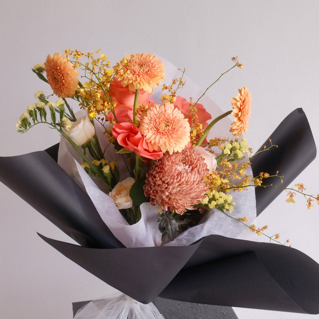 Bouquet of flowers orange rose, gerbera, and chrysanthemum wrapped in black paper with a white ribbon made by Hanaya Flora, Sydney, Surry Hills