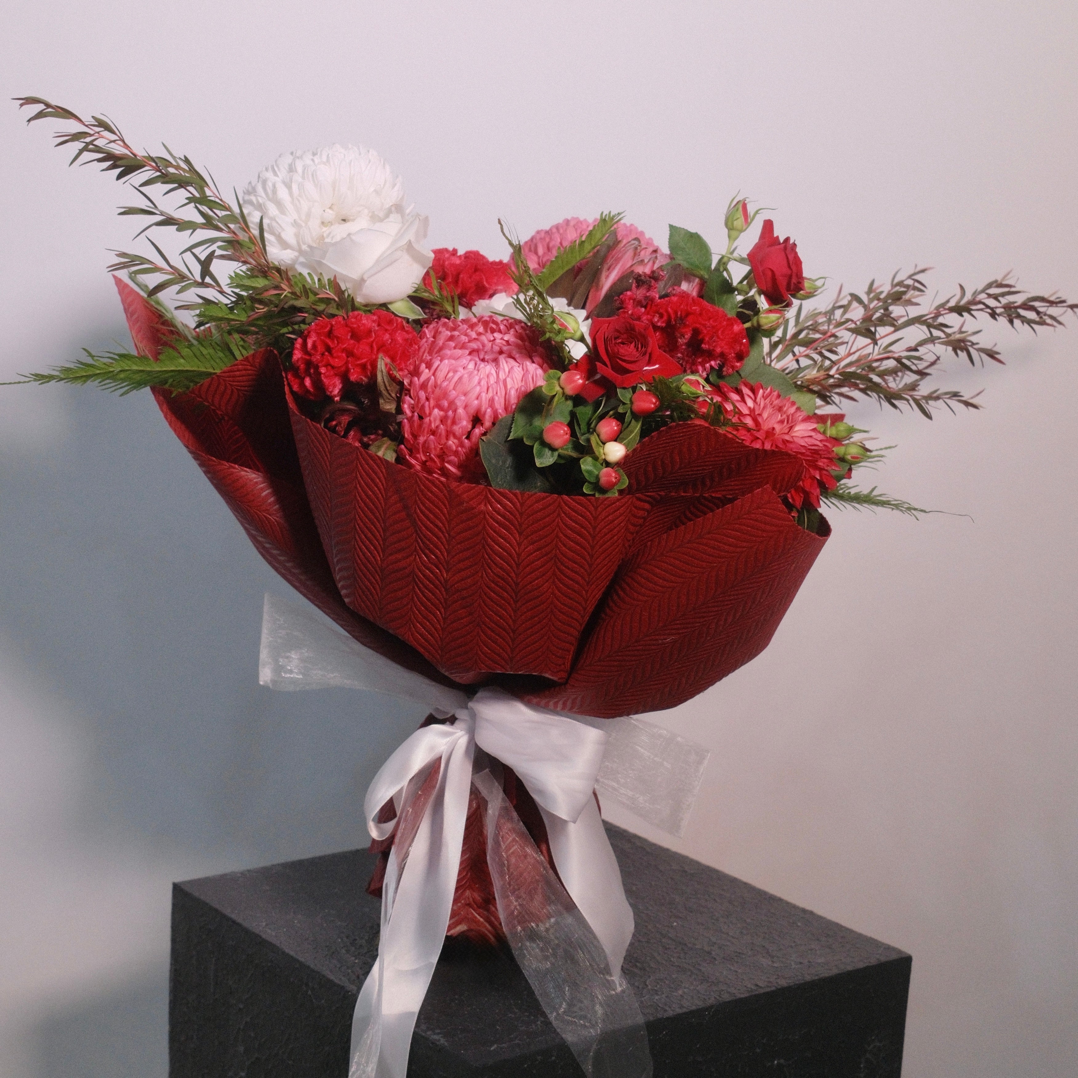 Bouquet of flowers roses, chrysanthemum, with red wrap and white ribbon by Hanaya Flora.