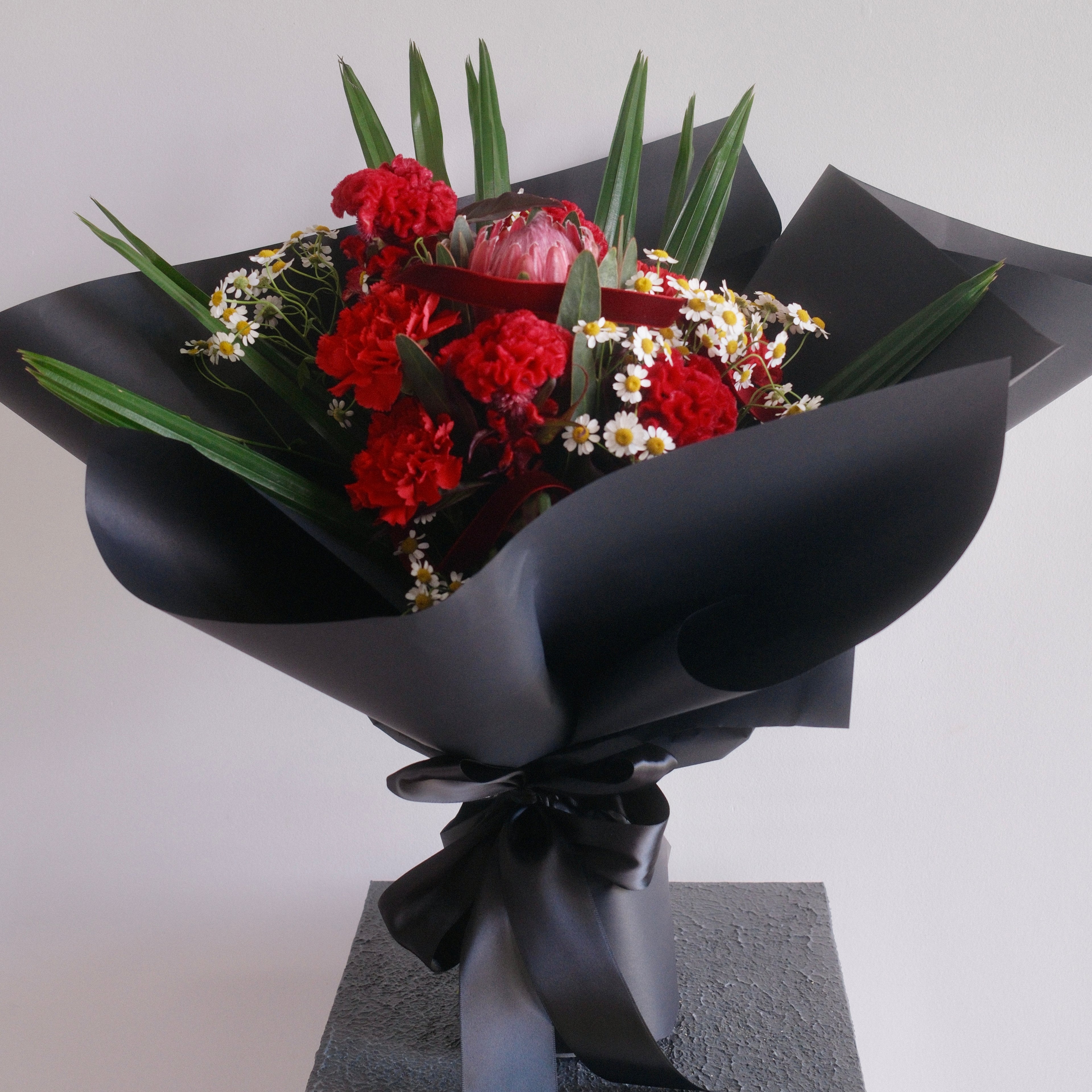 Bouquet of flowers with red carnation and chamomile, wrapped in premium black paper by Hanaya Flora, Surry Hills, Sydney. 