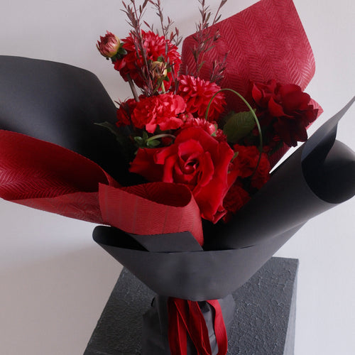 Bouquet of red flowers wrapped in black paper with a red ribbon, perfect for graduation gift ideas made by Hanaya Flora, based in Sydney.