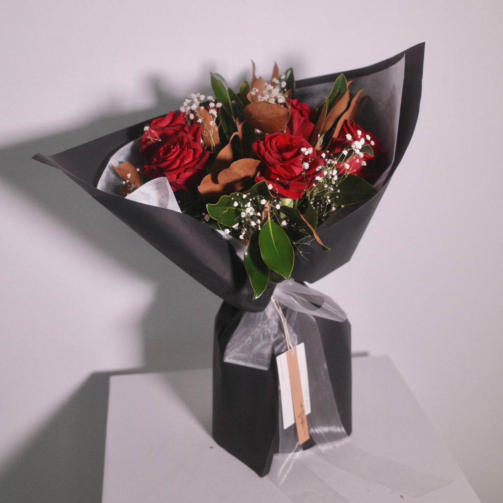Bouquet of red roses and magnolia leaves wrapped in black wrapping paper with a white ribbon by Hanaya Flora, Surry Hills