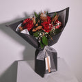 Bouquet of red roses and magnolia leaves wrapped in black wrapping paper with a white ribbon by Hanaya Flora, Surry Hills