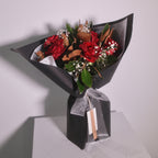 Bouquet of red roses and magnolia leaves wrapped in black wrapping paper with a white ribbon by Hanaya Flora, Surry Hills