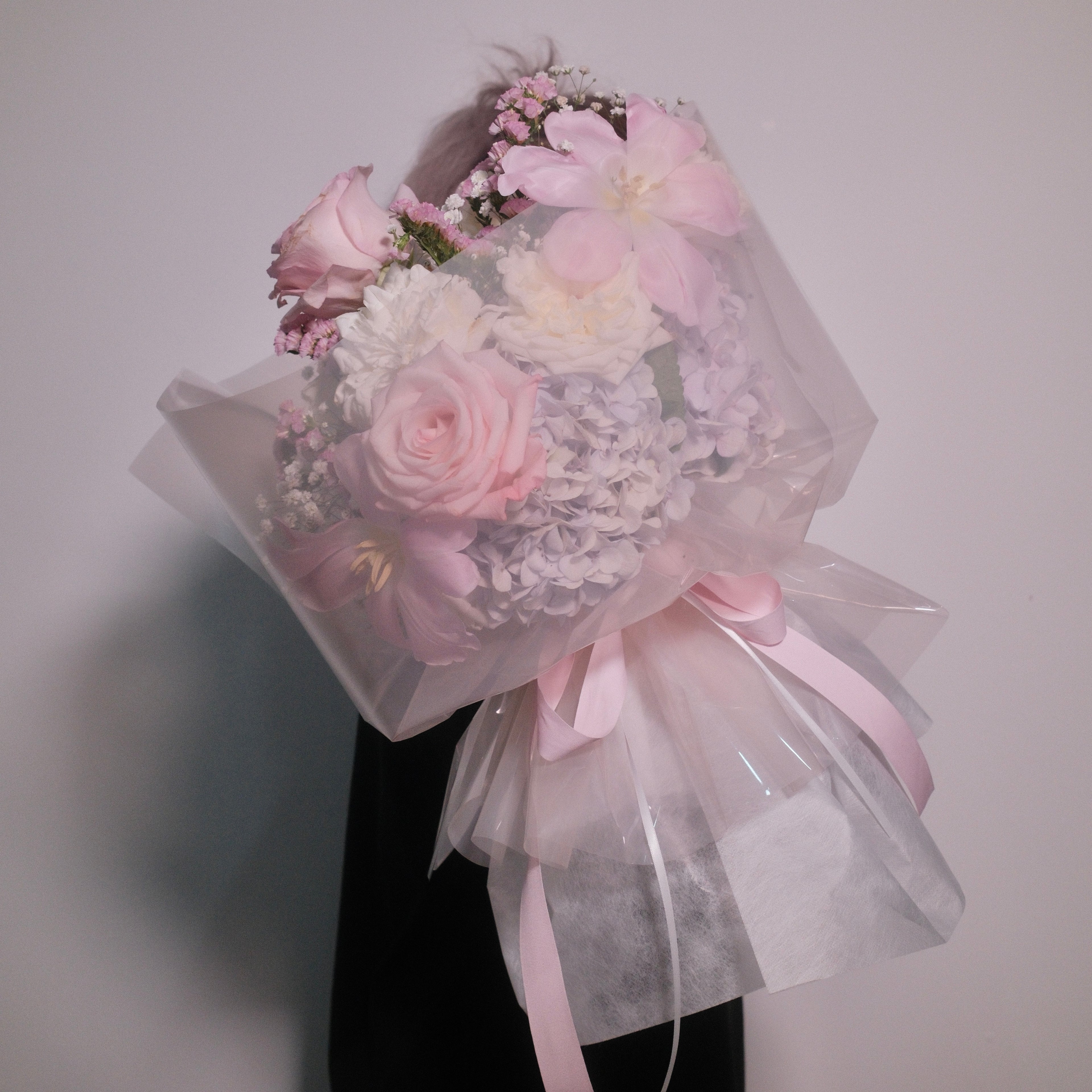 Cute bouquet of soft pink roses and delicate small white flowers with fluffy hydrangeas, wrapped in pink cellophane paper with a neat pink ribbon bow by Hanaya Flora, based in Sydney.
