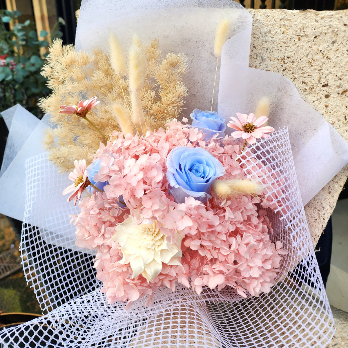 Close-up of Sakura Dream bouquet with pink preserved hydrangea, blue roses, ivory sola flower and bunny tail grass, Hanaya Flora
