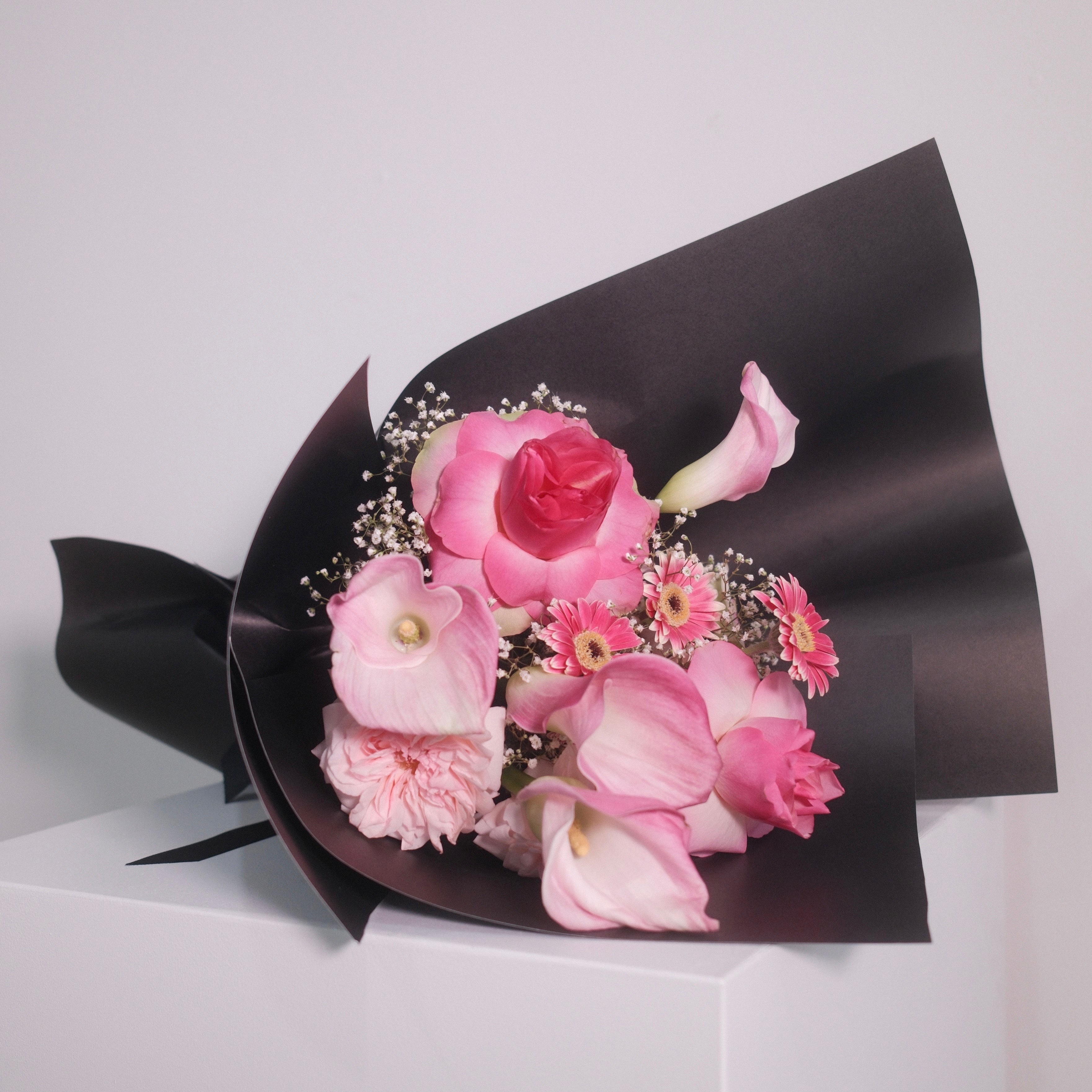 Sakura Veil bouquet with pink calla lilies, roses and gerbera daisies in a black wrap