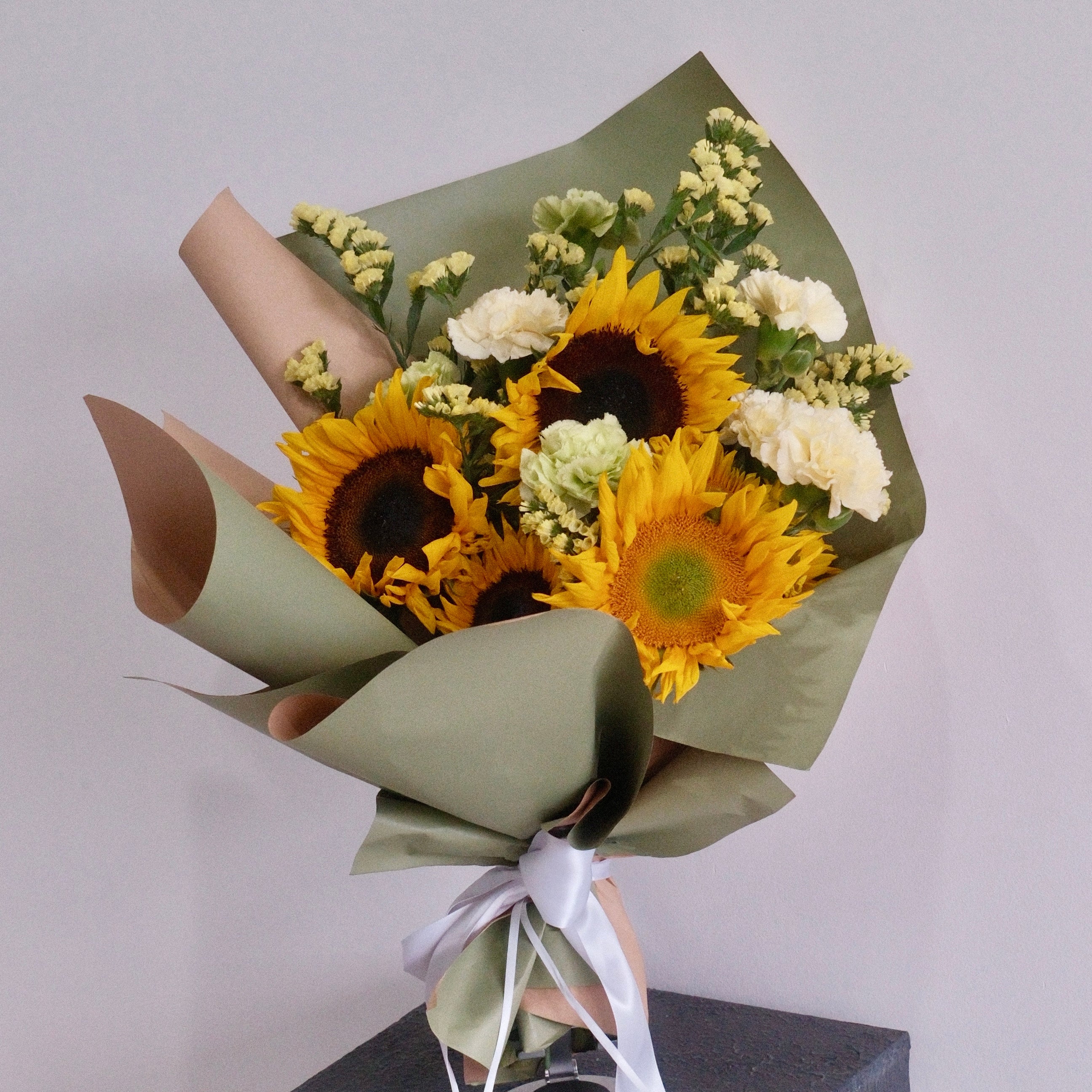 Bouquet of sunflowers and white flowers wrapped in green paper with a white ribbon, perfect for graduation flower gift delivered by Hanaya Flora, based in Sydney.