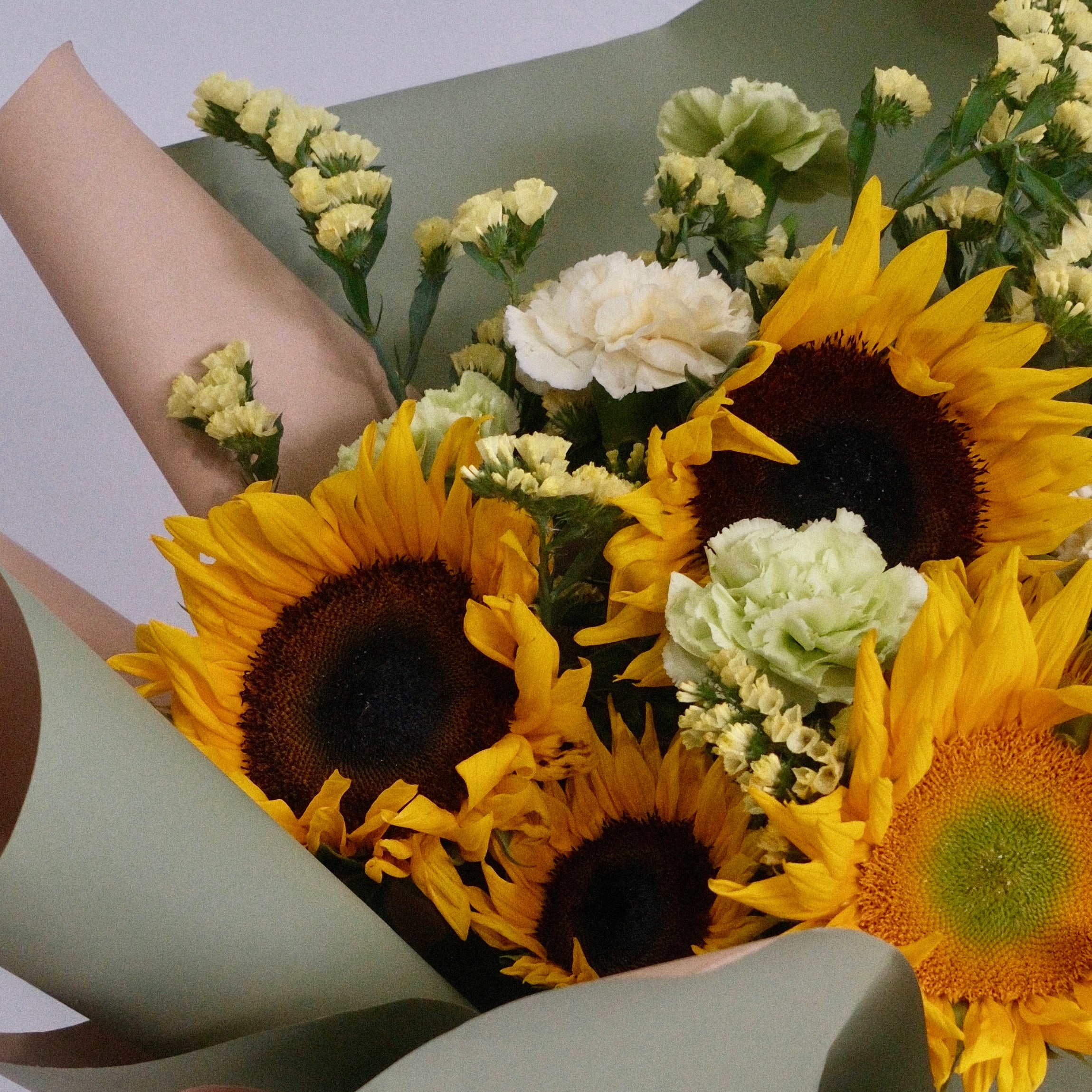 Bouquet of sunflowers and white flowers wrapped in green paper with a white ribbon, perfect for graduation flower gift delivered by Hanaya Flora, based in Sydney.